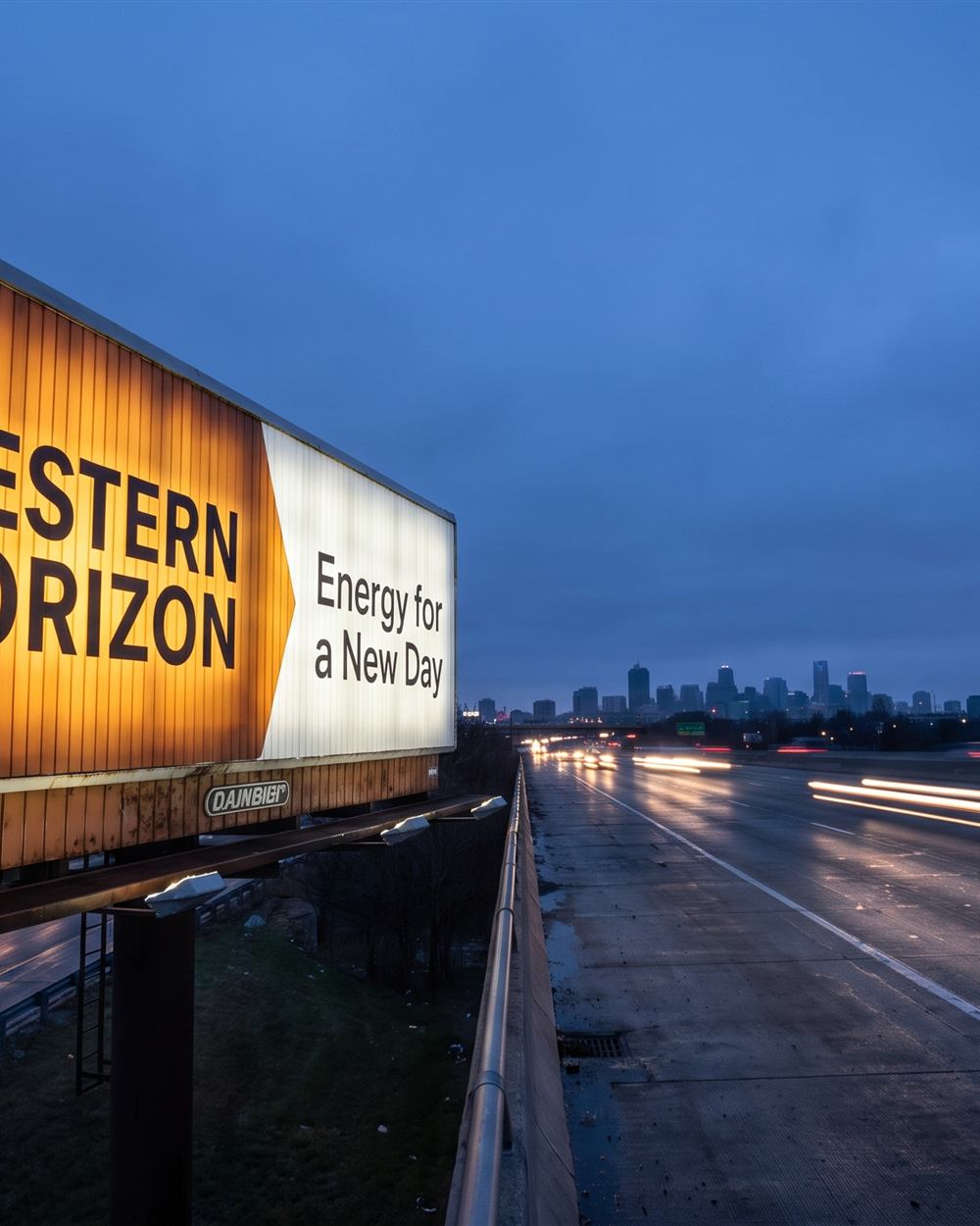 Highway bulletin billboard at dusk beside a multi-lane interstate