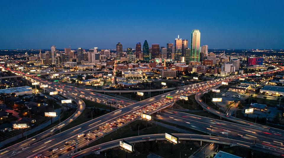 Aerial view of a city skyline at dusk with illuminated billboards along the highway